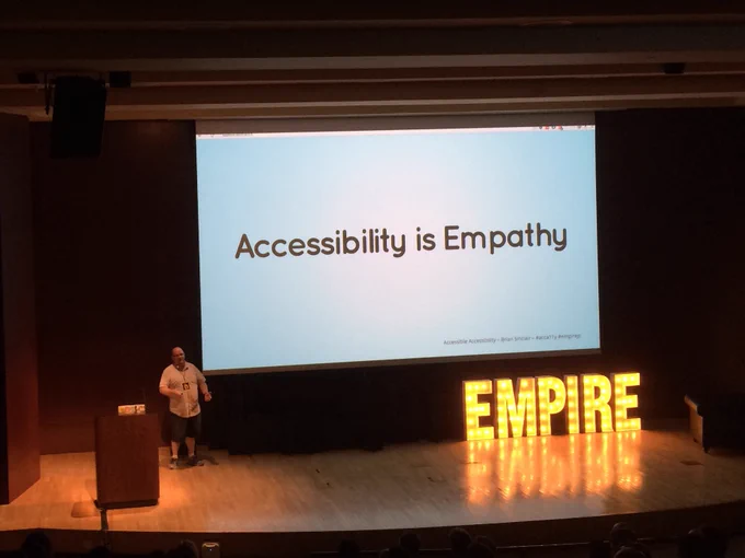 Speaker Brian Sinclair is on stage with a slide from his talk that says "Accessibility is Empathy"