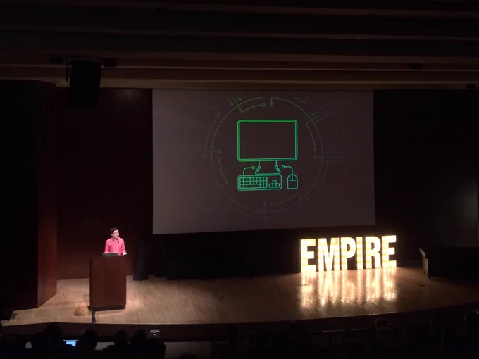Speaker Evan Morikawa on stage with a slide from his talk that has a line drawing on it of a desktop computer
