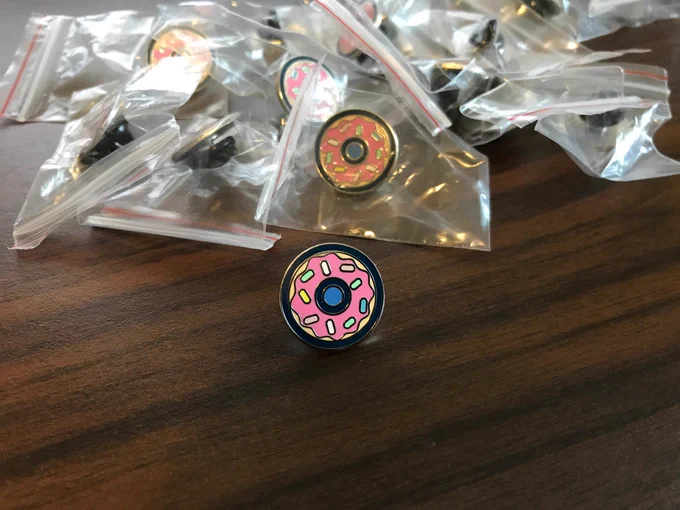A donut enamel pin on a desk surrounded by more pins.