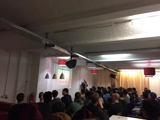 Room full of audience members with Öner presenting up front.