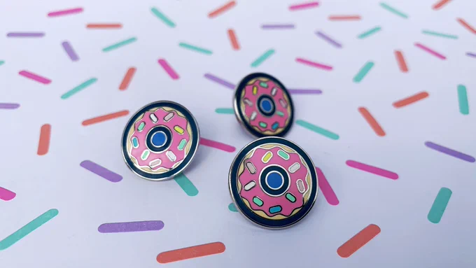Three donut enamel pins arranged on paper patterned with sprinkles.