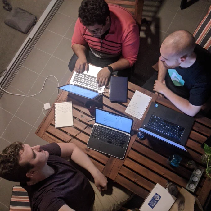 three dudes hunched over laptops at an outdoor table