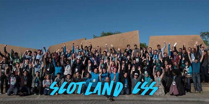 The diverse ScotlandCSS attendees standing with their hands up in the air for a group photo