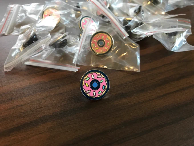 A donut enamel pin on a desk surrounded by more pins.
