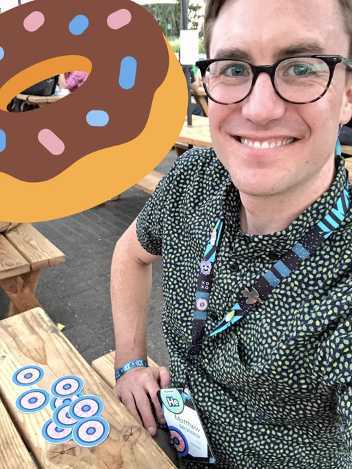 A selfie of a smiling person sitting at a picnic table. An array of donut stickers is on the table.