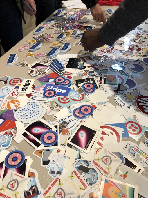 A table top full of hundreds of company stickers. A dozen or so Donut.js logo stickers are scattered atop the pile.