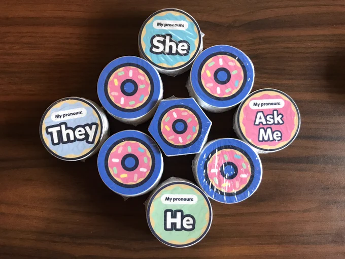 Stacks of round and hexagonal donut stickers and several pronoun stickers (Ask Me, He, She, They)
