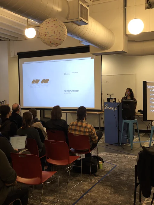 A person standing at a podium giving a talk to a room full of people. There is a projection screen next to them with examples of poetry written on it.