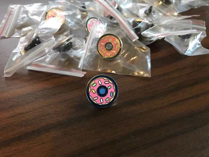 A donut enamel pin on a desk surrounded by more pins.