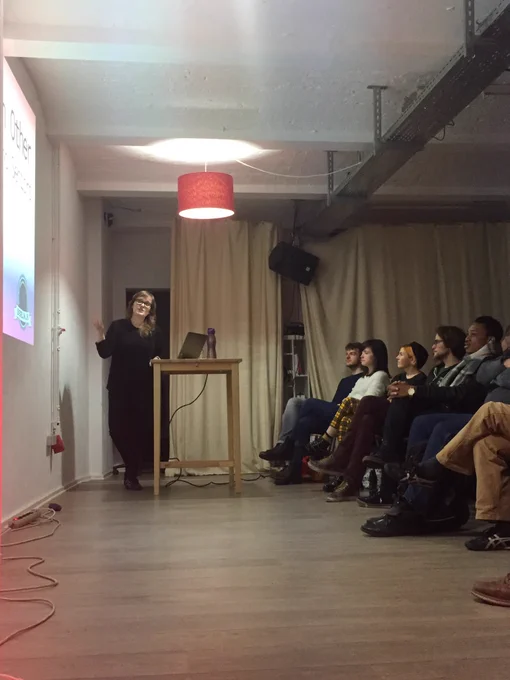 Lara on stage pointing at the screen. A full front row of alert attendees.