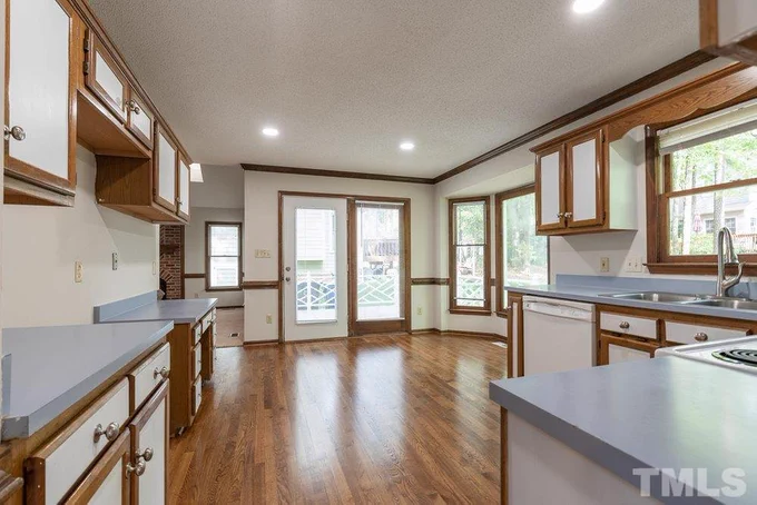 A large kitchen with wood floors and wood trim on every single feature. Cabinets, windows, the crown molding, the baseboards. All of it is wood outlined.