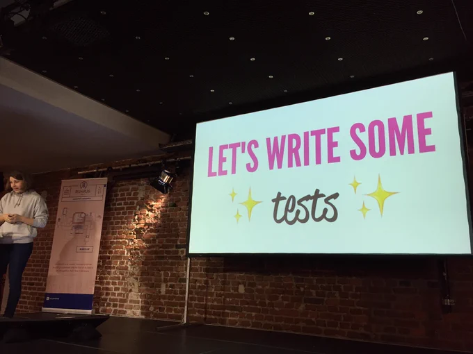 Mirjam on Stage with a slide that says “let’s write some tests”.