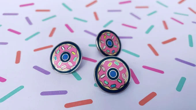 Three donut enamel pins arranged on paper patterned with sprinkles.