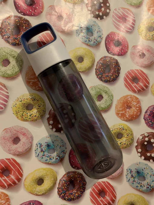 A tall, tinted water bottle laying on a background of donut wrapping paper.