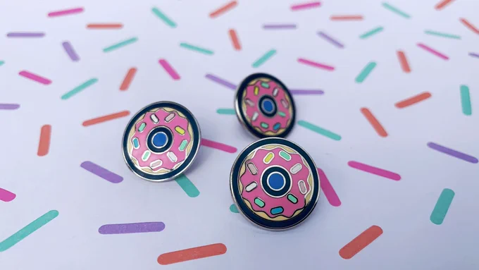 Three donut enamel pins arranged on paper patterned with sprinkles.