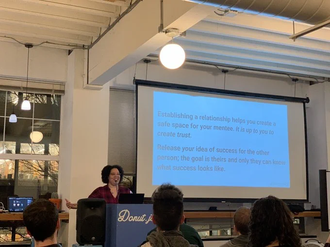 A person giving a talk at a podium in front to a room full of people in chairs. Behind the speaker is a projector screen with the words:
Establishing a relationship helps you crate a safe space for your mentee. It is up to you to create trust.
Release your idea of success for the other person; the goal is their and only they can know what success looks like.