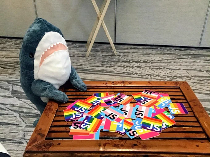 a pile of lgbtq flag stickers being looked over by a plush shark