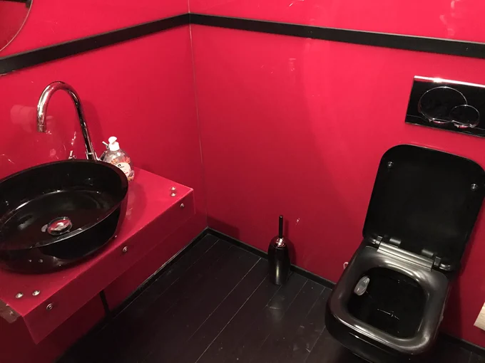 A bathroom with red walls and counters but black toilet and sink.
