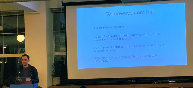 A person giving a talk at a podium in front to a room full of people in chairs. Behind the speaker is a projector screen:
• Accessibility is important
• JS can alleviate a lot of the costs preventing people from making their podcasts accessible
• JS isn’t perfect, and accessibility effects still require human intervention
• Involve people in your accessibility project who will be affected by it