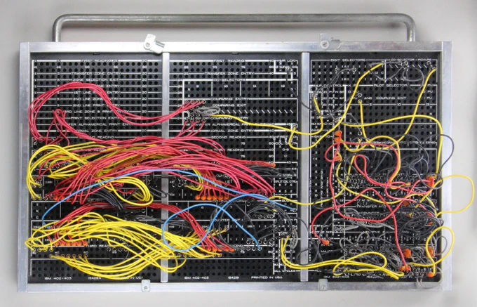 A plugboard, with many colorful wires plugged into it. It has a carrying handle at the top.