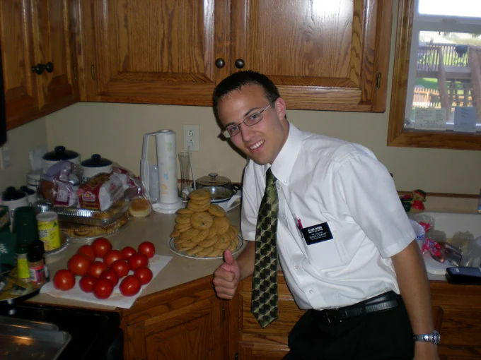 Kent as a missionary giving thumbs up in a kitchen with a plate piled full of cookies