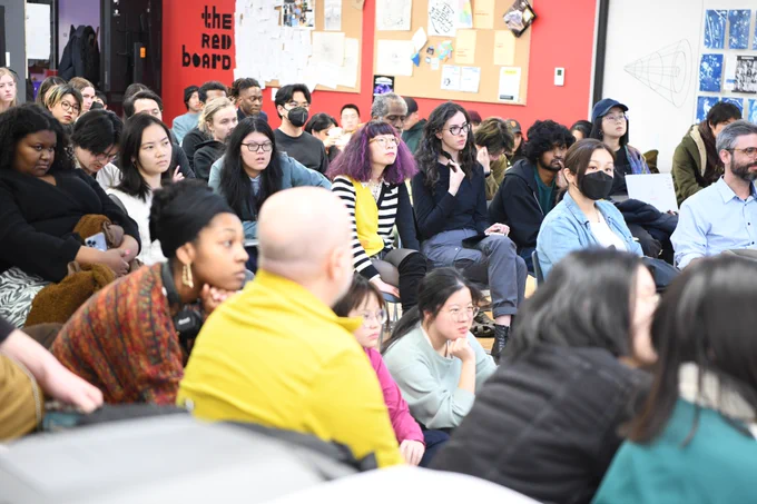 An image of the p5 salon audience members. People are sitting in a crowded room with curious and serious expressions
