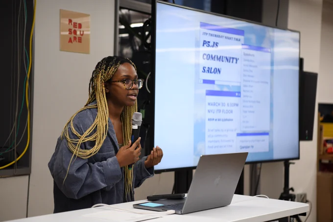 An image of Olivia Ross holding a mic next to a big t.v. screen that has the p5 salon poster on it.
