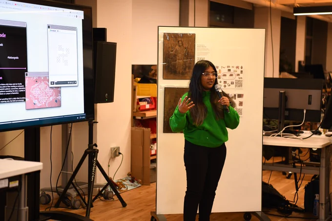 An image of Lavanya Suresh holding a mic next to a big t.v. screen that has an image of her work on Kolams
