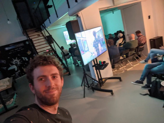 Selfie of me at a meetup. Screens are showing the TypeScript documentary scene containing a view of my back as I code at a standing desk