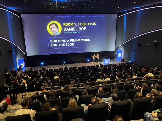 Elena and Ramón introducing a speaker in the stage. The picture is taking from the end of the room, so the audience appears as well.