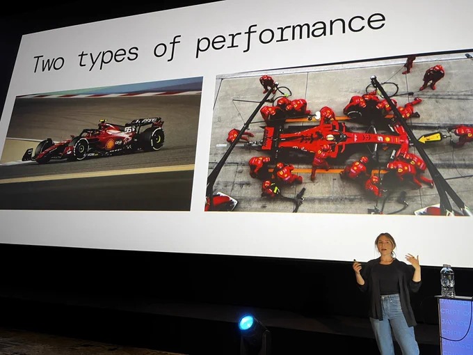 Aleksandra on stage presenting. Slide behind shows formula on track and in cockpit.

“Two types of performance” is written in the title