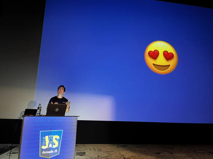 Sergio presenting on stage. Behind him a blue screen with heart-eye smiley