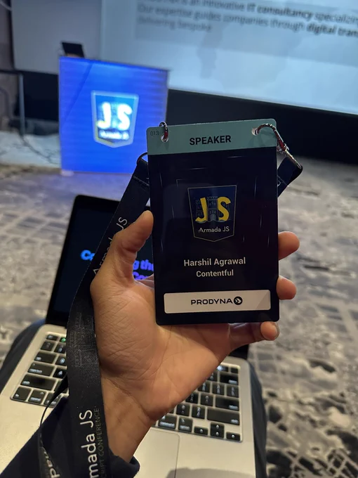 Conference speaker badge with my name and name of my employer. In the background my machine displaying my slides.