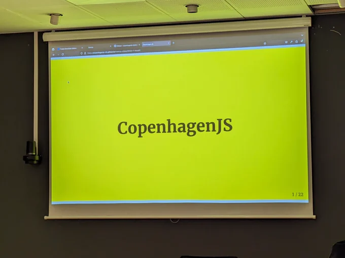 A projector screen with CopenhagenJS in black text on a yellow background.