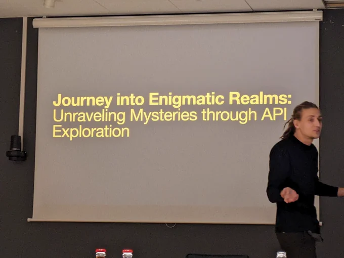 Person in front of a screen that says "Journey into Enigmatic Realms: Unraveling Mysteries through API Exploration"
