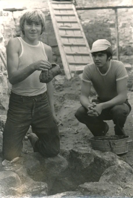 Egils Jemeļjanovs (no labās) un Jānis Ciglis pie 1982. gada izpētes laikā atraktās mazās “aciņas”, kurā iekšā tika uziets viens no tās vasaras ievērojamākajiem atradumiem – akmensmasas keramikas krūze. (14.gs.).