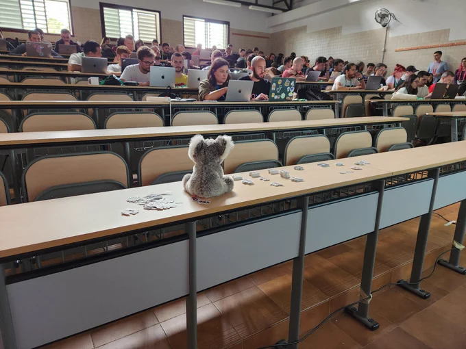 A classroom with 60 people working on their laptops and a Koala plush toy in front of them