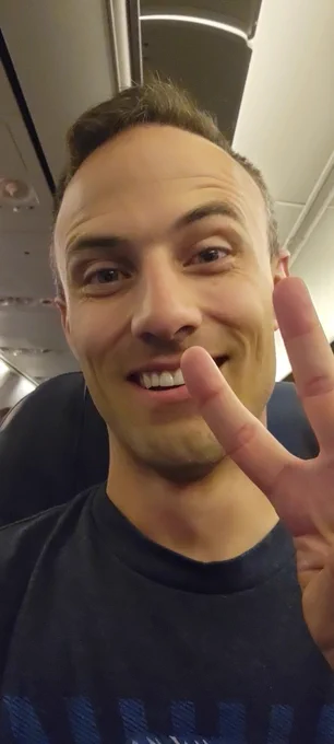 Kent in an airplane seat giving a peace sign