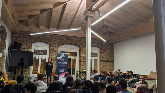 A woman wearing black on the stage of GreeceJS meetup presenting our sponsor for the 48th meetup Coded Lines, an end-to-end mobile and  web app development and digital marketing agency.