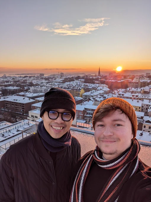 Thang and I taking a selfie over an Oslo sunset from a rooftop. The sky is clear, the air is crispy - 20°C. The roofs are snowy.