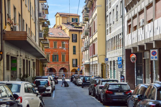 People of all ages and abilities walk, cycle, drive, and ride public transportation along the low-traffic streets of Bologna, which are lined with buildings, trees, bike infrastructure, and prominent 30 km/h speed limit signage and road markings.