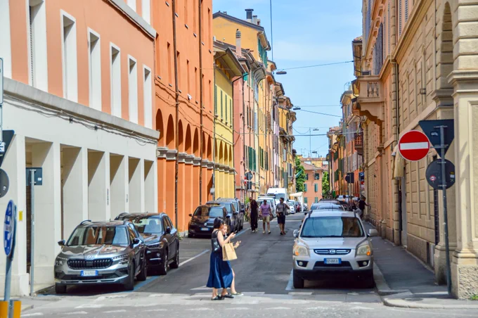 People of all ages and abilities walk, cycle, drive, and ride public transportation along the low-traffic streets of Bologna, which are lined with buildings, trees, bike infrastructure, and prominent 30 km/h speed limit signage and road markings.
